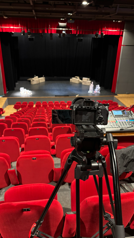 Prestations complémentaires Scène de théâtre avec des sièges rouges et une caméra sur trépied au premier plan.