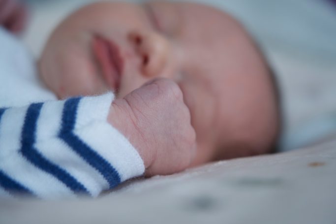 Photo Bébé endormi avec un poing fermé, portant un vêtement à rayures.